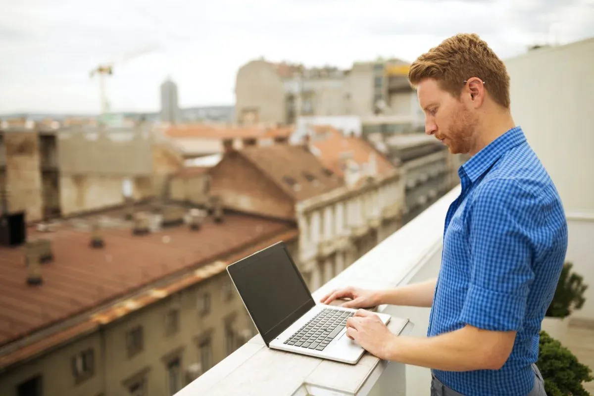 Man working on a laptop on a rooftop terrace above the city