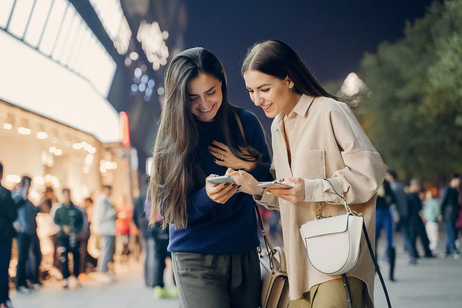 Two women looking at a phone together on a busy shopping street at night