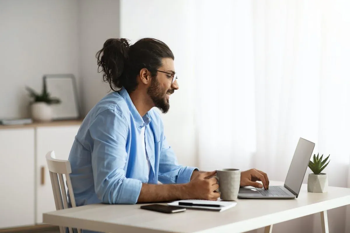 Man working on a laptop with a coffee at a home office desk