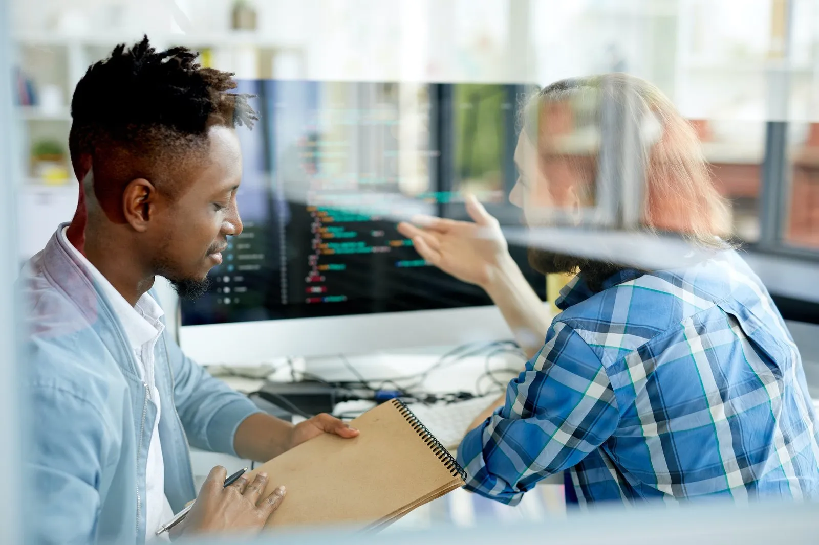 Two colleagues discussing work in front of a screen of code