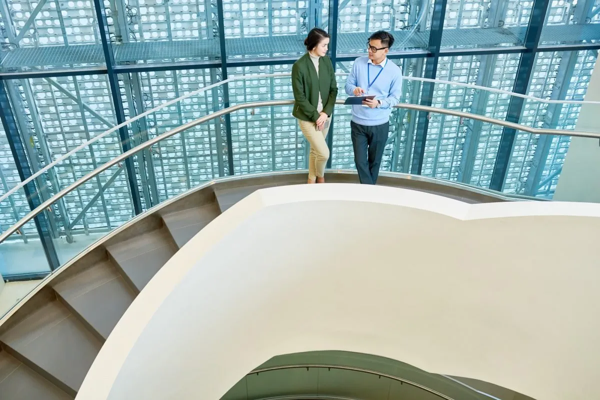 Two colleagues talking on a spiral staircase in a glass atrium