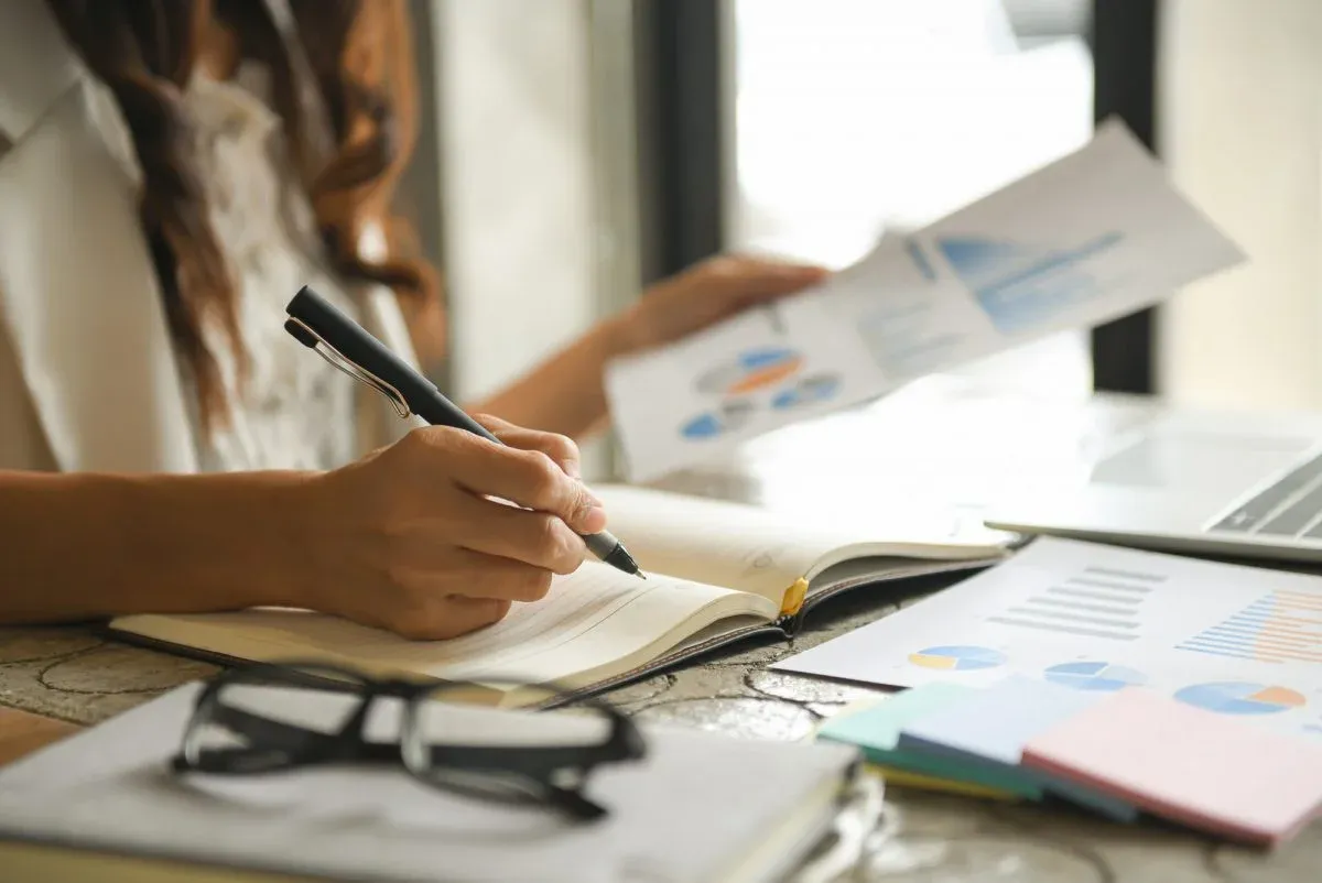 Person making notes beside printed charts and reports