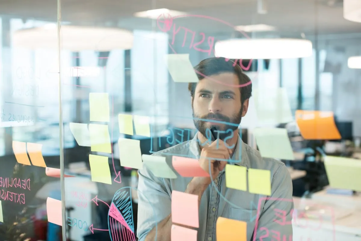 Man thinking behind a glass wall covered in sticky notes