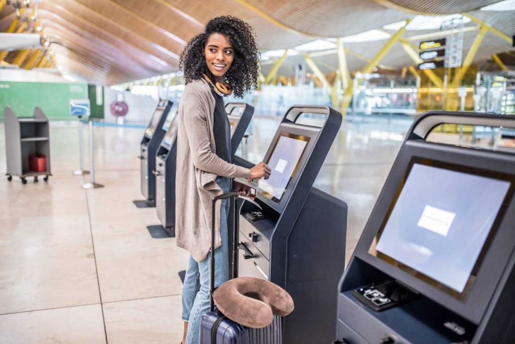 happy black woman using the check-in machine at the airport gett