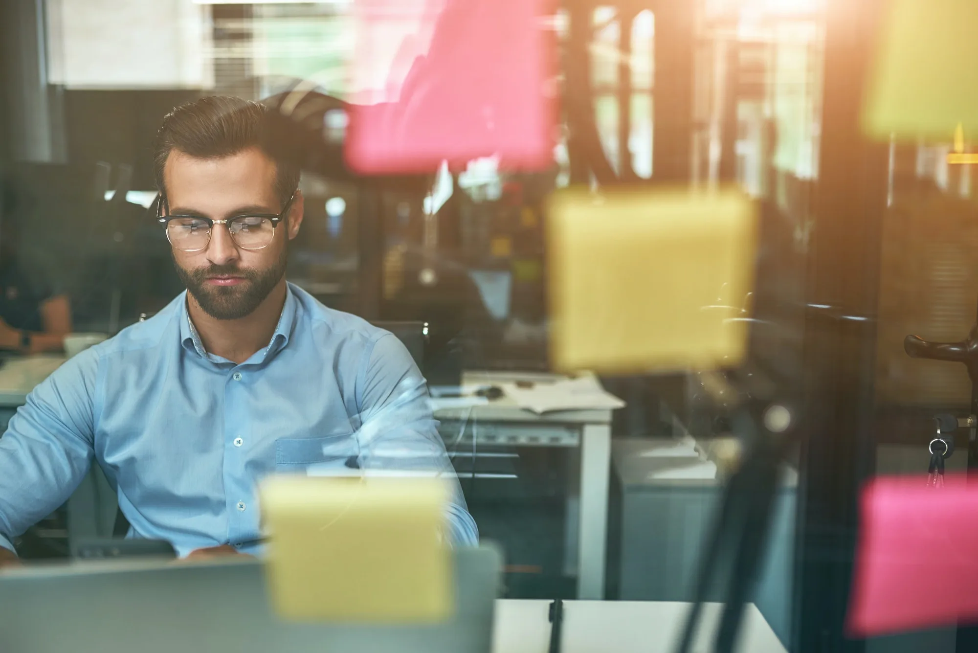Project management. Young focused businessman in eyeglasses working while sitting at office in front