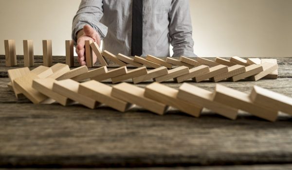 Hand stopping domino effect of wooden blocks