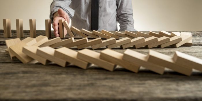 Hand stopping domino effect of wooden blocks