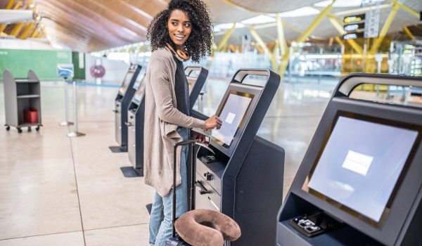 happy black woman using the check-in machine at the airport gett