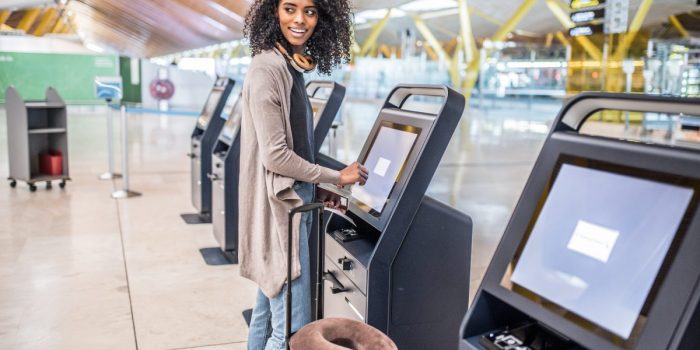 happy black woman using the check-in machine at the airport gett