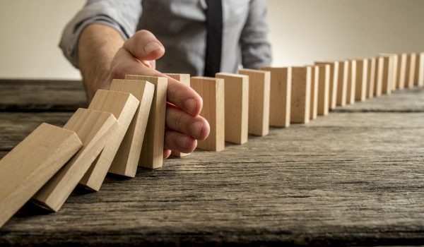 Man stopping domino effect on wooden table