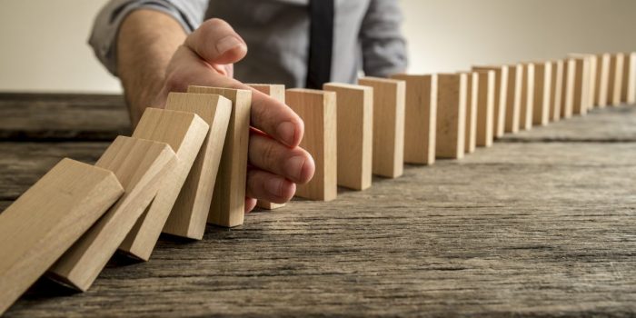 Man stopping domino effect on wooden table
