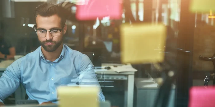 Project management. Young focused businessman in eyeglasses working while sitting at office in front