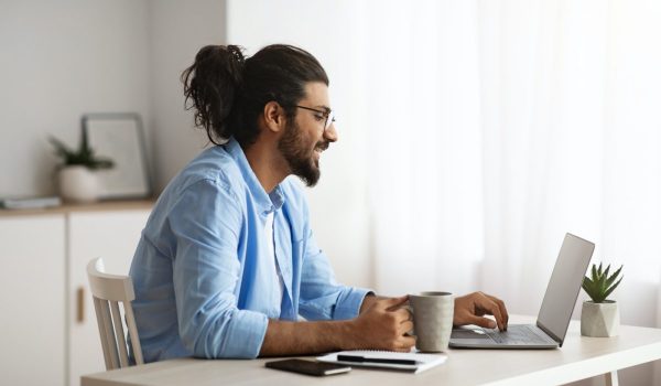 Remote Work. Male Freelancer Using Laptop And Drinking Coffee At Home Office