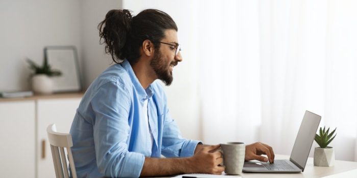 Remote Work. Male Freelancer Using Laptop And Drinking Coffee At Home Office